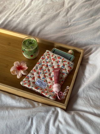 Image of a desk laid out with lots of items including our astala luna pouch, a passport, lipbalm, camera, book, hair clip and airpods.